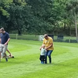 Adults and children running a 3-legged race on grass